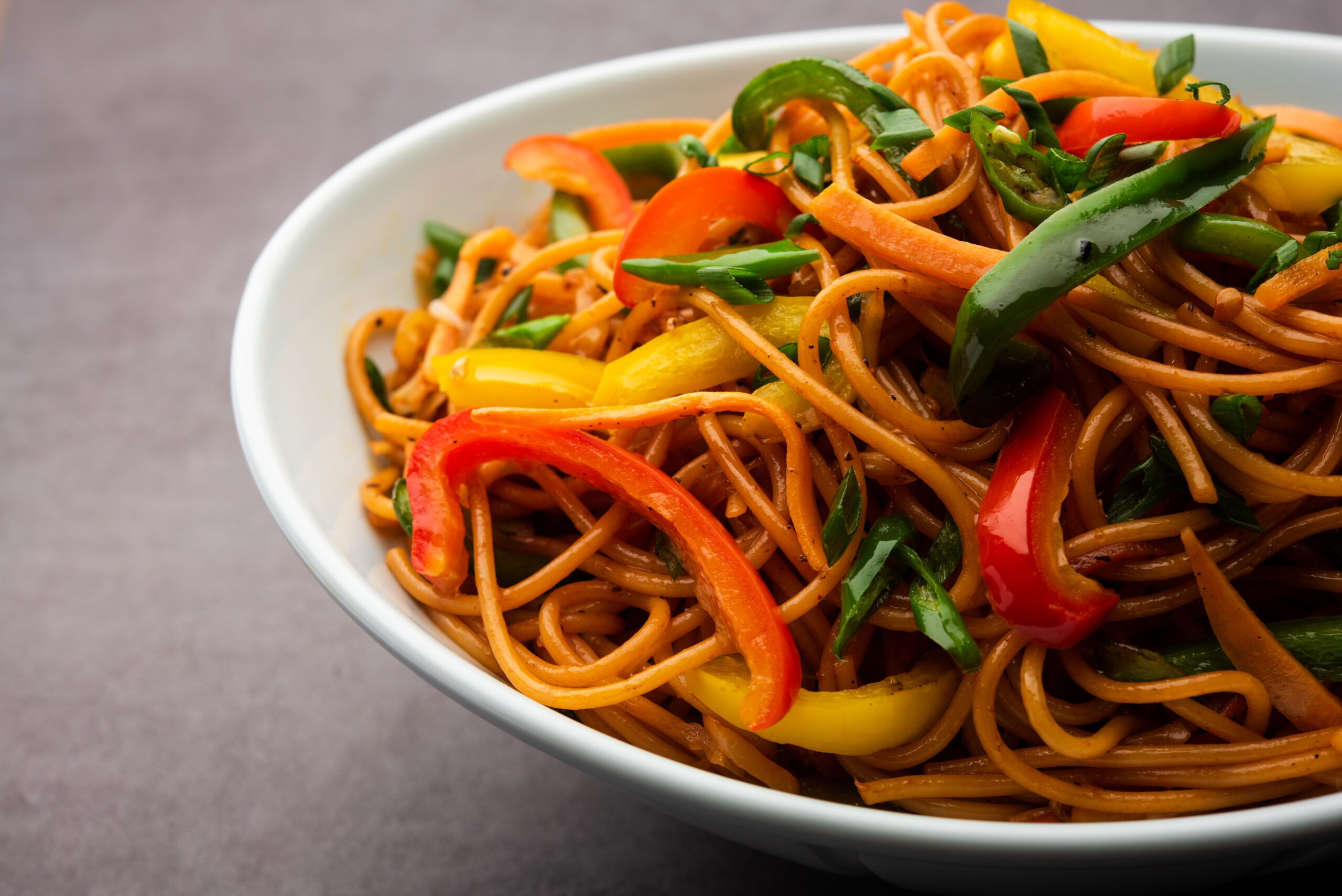 Schezwan Noodles or Szechwan vegetable Hakka Noodles or chow mein is a popular Indo-Chinese recipes, served in a bowl or plate with wooden chopsticks